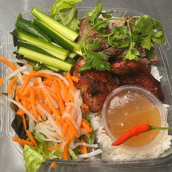 Vietnamese grilled chicken and beef with rice, pickled carrots, daikon, cucumbers, and sauce in a to-go container.