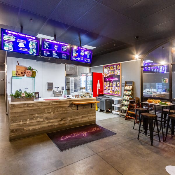 Interior of La Baguette Vietnamese Sandwiches, showing the counter, menu screens, and seating area.