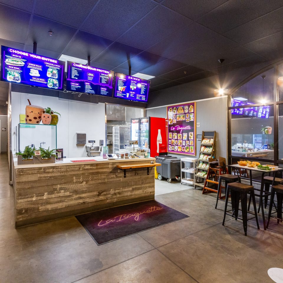 Interior of La Baguette Vietnamese Sandwiches, showing the counter, menu screens, and seating area.